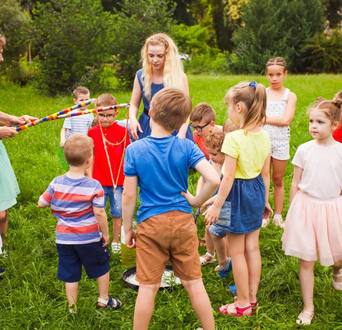 Un groupe d'enfants réunis en cercle dans l'herbe autour d'une animatrice